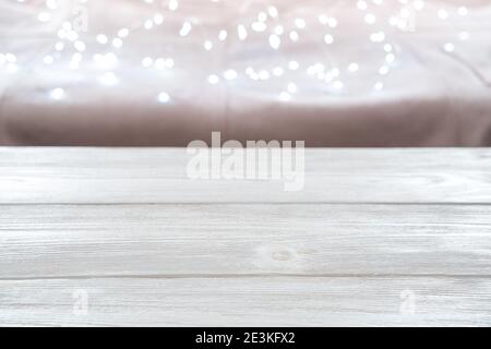 Festive background, empty, blurred wooden white table on the background of a twinkling garland. Stock Photo