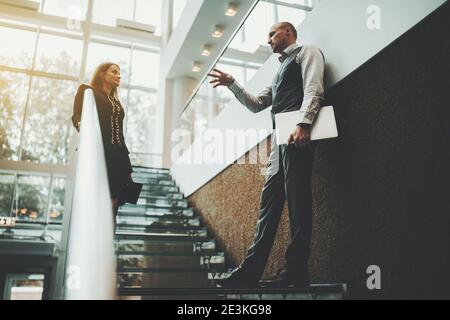 A scene on the stairs of a modern luxury office skyscraper with a selective focus on an actively gesticulating man entrepreneur with a laptop explaini Stock Photo