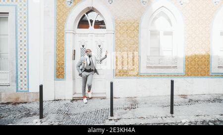 A stylish mature bald black guy with a well-groomed beard is leaning against an entrance doorjamb while standing on the stoop of a beautiful Portugues Stock Photo