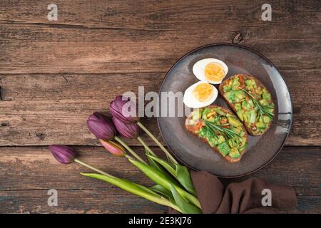 Toast with avocado, eggs and tulips on a wooden background. Stock Photo