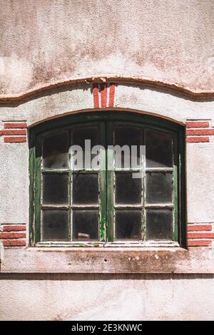 A vertical shot of an old wooden leaded window with peeling green paint and with a part of plastered reddish wall of an antique European house, fake r Stock Photo