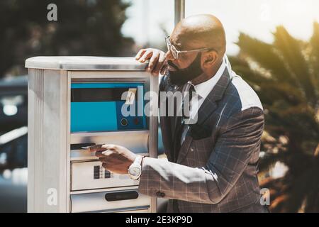 A portrait of a mature elegant black man entrepreneur with a well-groomed beard, in eyeglasses and a fashionable custom plaid grey suit, inserting a c Stock Photo