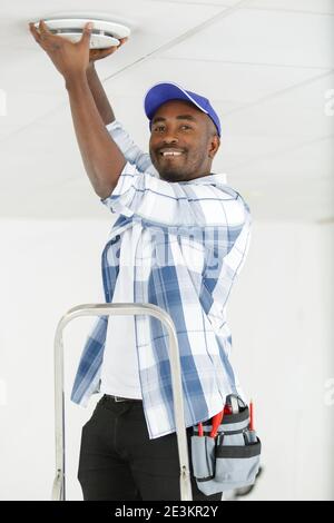 man using screwdriver to install smoke detector on ceiling Stock Photo