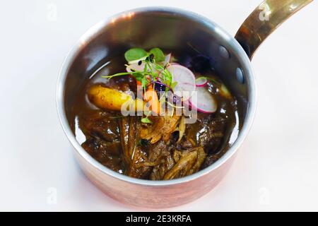 slow cooked pulled lamb shoulder in a coper pot with baby carrots and slice radish Stock Photo