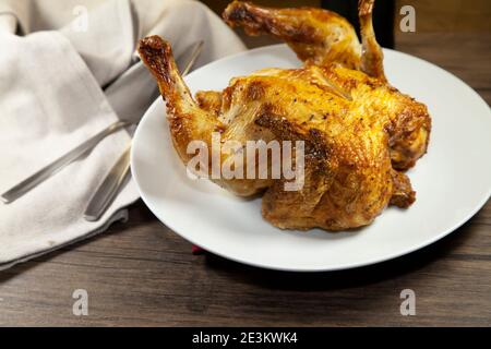 Whole roasted chicken on a white plate next to a grey napkin and silverware Stock Photo
