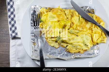 Vegetarian omlet with broccoli on silver foil on a white plate with silverware on a white napkin with a blue and white checkered border Stock Photo