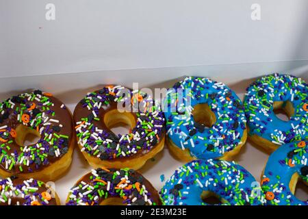 Donuts with brown and blue icing covered with multicolored sprinkles in a white box on a wooden table Stock Photo