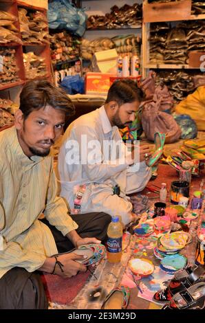 Two workers paint leather khussa shoes with colors and materials at workshop Karachi Pakistan Stock Photo