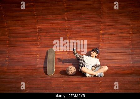 teenage asian skateboarder boy taking a selfie using mobile phone Stock Photo