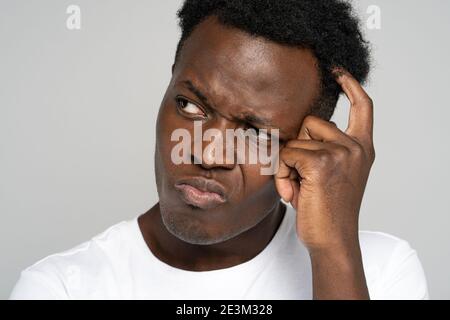 Unsure doubtful Black man scratching head, looking left doubtfully, plans or reconsiders something Stock Photo