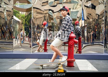 teenage asian boy with skateboard leaning against fire hydrant on street Stock Photo