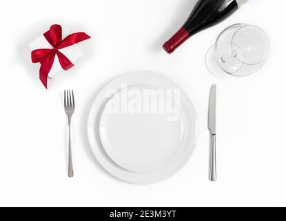 Festive table setting with a gift, wine and dishes on a white background. Romantic dinner concept for Mothers Day, Valentines Day and Christmas. Stock Photo