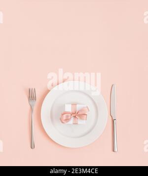 Festive table setting for Valentines Day, Mothers Day, Birthday or Christmas. Gift in a plate on a pastel pink background. Minimal concept. Stock Photo