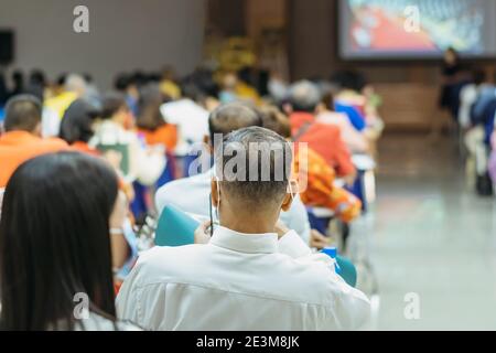 Back view of Asian man wear protective face mask to prevent Coronavirus(COVID-19) sitting on a chair for social distancing in  auditorium. Conference Stock Photo