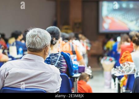 Back view of Asian man wear protective face mask to prevent Coronavirus(COVID-19) sitting on a chair for social distancing in  auditorium. Conference Stock Photo