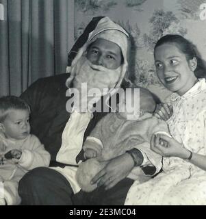 A young mom grinning with her two kids and Santa Claus, circa 1960 Stock Photo