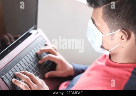 rear view of young man in surgical mask using laptop  Stock Photo