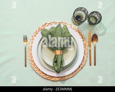 Beautiful festive table setting in green colors for St.Patrick's day with golden cutlery. Top view of Saint Patrick's day holiday table with green linen tablecloth and napkin, green glasses. Flat lay Stock Photo