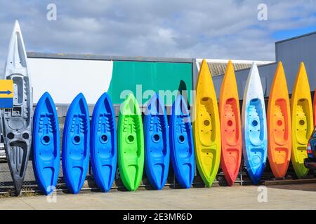A row of plastic kayaks of various colors and sizes, lined up along a fence Stock Photo