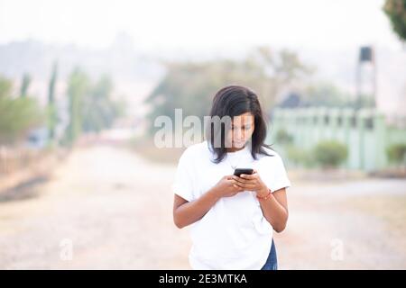 beautiful light skin african lady using her phone outdoors while walking Stock Photo