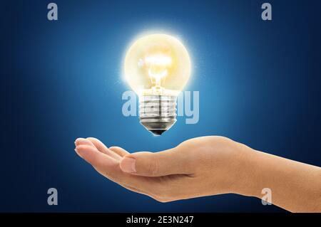 Glowing light bulb floating over an open hand against a blue background Stock Photo
