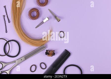 Hair styling concept with dark blond hair, elastic hair ties, hair pins, comb and thinning shears on purple background with empty copy space on side Stock Photo