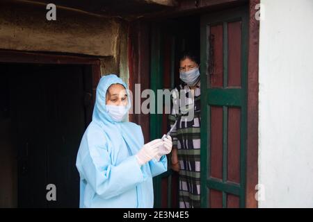 Young woman doctor in PPE protective mask and gloves holding a syringe and coronavirus vaccine, standing with village women explaining importance of c Stock Photo