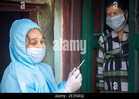 Young woman doctor in PPE protective mask and gloves holding a syringe and coronavirus vaccine, standing with village women explaining importance of c Stock Photo