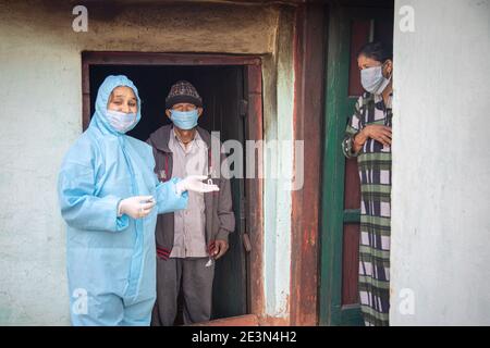 Young woman doctor in PPE protective mask and gloves holding a syringe and coronavirus vaccine, standing with village man and women explaining importa Stock Photo