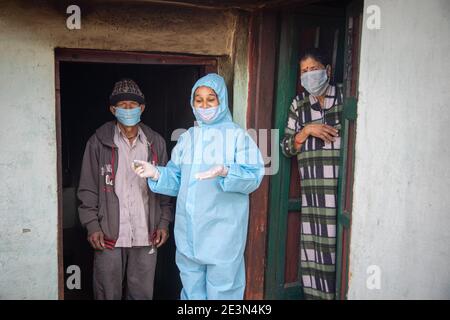 Young woman doctor in PPE protective mask and gloves holding a syringe and coronavirus vaccine, standing with village man and women explaining importa Stock Photo