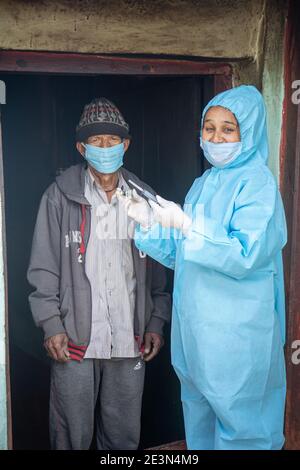 Young woman doctor in PPE protective mask and gloves holding a syringe and coronavirus vaccine, standing with village men explaining importance of cor Stock Photo