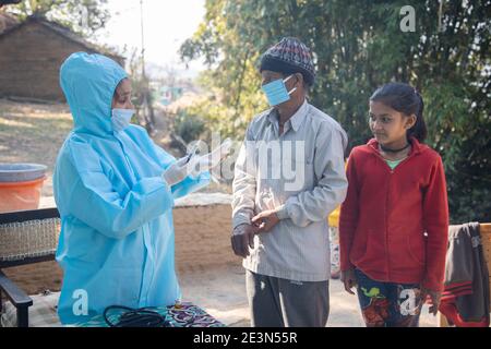 Young woman doctor in PPE protective mask and gloves holding a syringe and coronavirus vaccine, standing with village people explaining importance of Stock Photo