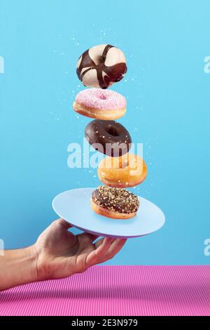 Hand holding plate with flying donuts on pink and blue background. Stock Photo