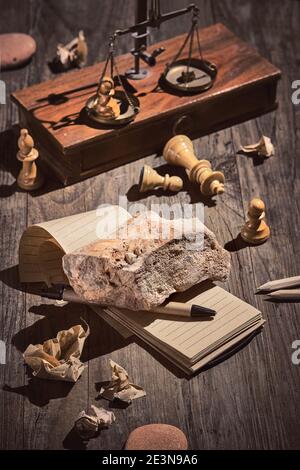 Writer Block. Concept still life, arrangement on dark wooden table. Heavy stone, brick on open blank block note. Crumpled paper. Chess figures, stones Stock Photo