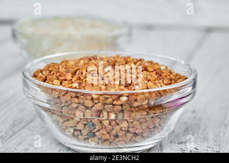 Raw white rice and buckwheat groats in a transparent glass plate on wooden background. Closeup. Stock Photo