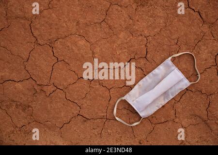 Waste during COVID-19. Discarded on cracked ground. Trash on dry soil texture coronavirus single-use face masks. Environmental pollution. Stock Photo