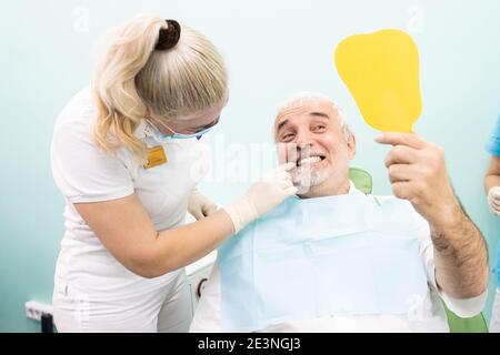 Dentistry concept. Professional dental services and modern equipment without pain. A doctor consults and treats an elderly man. The patient looks in Stock Photo