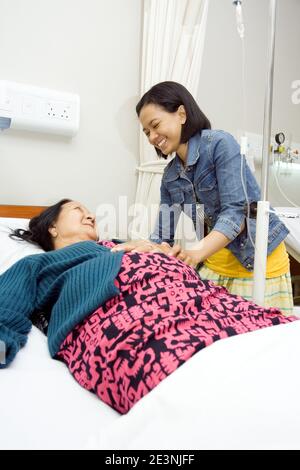 A Southeast Asian granddaughter visit her sick grandmother having bedrest for inpatient treatment at hospital Stock Photo