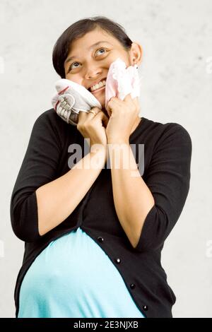 pregnant asian woman with pairs of baby shoes. looking up and wondering whether she is going to have a baby boy or a girl or twin Stock Photo