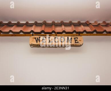brown roof with a wooden carte that says "welcome" hanging from the with white wall Stock Photo