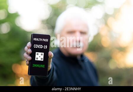 Senior man showing an vaccination certificate on a mobile phone, which indicates a vaccination against covid-19. Stock Photo