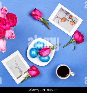 Easter eggs, red roses, a cup of black coffee and Easter pictures on blue background Stock Photo