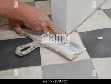 A building contractor installing linoleum flooring near the drywall partition wall is cutting along the crease of black and white linoleum. Stock Photo