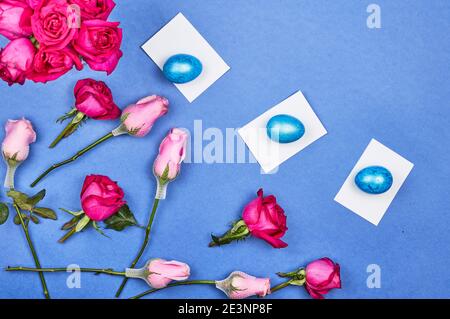 Easter eggs, red rose flowers, a cup of black coffee on blue background Stock Photo