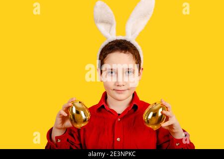 Cute boy in bunny ears headband holding Golden Easter eggs Stock Photo