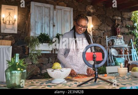 African senior woman streaming online virtual masterclass cooking lesson outdoors at home - Focus on face Stock Photo