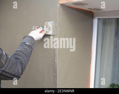 A DIYer, homeowner or professional is applying the final coat of render within the window area using spatula in the external wall insulation process. Stock Photo