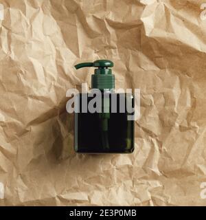 Green glass soap dispenser bottle on crumpled paper, top view. Stock Photo