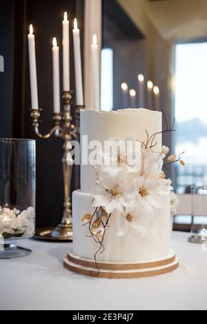 White wedding cake decorated with flowers and candles in the background Stock Photo