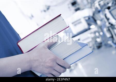 Books stacked in the hands of a young specialist in a room with equipment Stock Photo